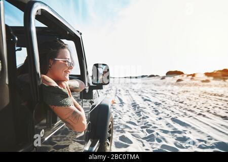 Giovane donna sorridente che si appoggia fuori dalla finestra di jeep, godendo il viaggio in spiaggia Foto Stock