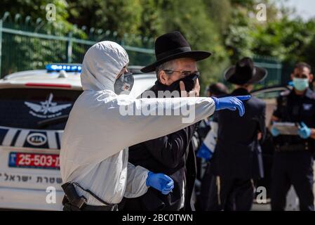 Bnei Brak, Israele. 02nd Apr, 2020. Un poliziotto israeliano in tuta conduce un uomo ebraico ortodosso, fuori dal Ponevezh Yeshiva, un'istituzione ebraica che si concentra sullo studio dei testi religiosi tradizionali, dove lui e altri insistono a portare avanti la loro preghiera nonostante il blocco imposto in mezzo alla pandemia del coronavirus. Credit: Ilia Yefimovich/dpa/Alamy Live News Foto Stock