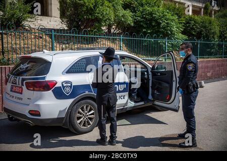 Bnei Brak, Israele. 02nd Apr, 2020. Un poliziotto israeliano si trova accanto ad un ebreo ortodosso di fronte al Ponevezh Yeshiva, un'istituzione ebraica che si concentra sullo studio dei testi religiosi tradizionali, dove lui e altri insistono a portare avanti la loro preghiera nonostante il blocco imposto in mezzo alla pandemia del coronavirus. Credit: Ilia Yefimovich/dpa/Alamy Live News Foto Stock