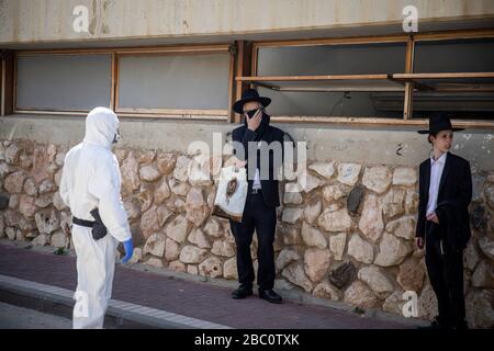 Bnei Brak, Israele. 02nd Apr, 2020. Un poliziotto israeliano in tuta ferma gli ebrei ortodossi, che insistono a portare avanti con la loro preghiera al Ponevezh Yeshiva, un'istituzione ebraica che si concentra sullo studio dei testi religiosi tradizionali, nonostante il blocco imposto in mezzo alla pandemia del coronavirus. Credit: Ilia Yefimovich/dpa/Alamy Live News Foto Stock