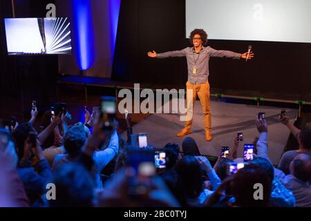 Pubblico con telefoni con fotocamera che fotografa un altoparlante entusiasta sul palco Foto Stock