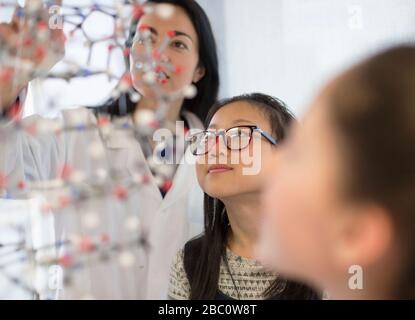 Insegnante di sesso femminile e studentesse curiose che esaminano la struttura molecolare in classe di laboratorio Foto Stock