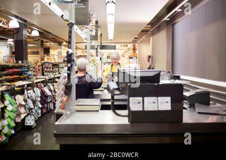 Cassa femminile senior che aiuta il cliente al checkout del supermercato Foto Stock