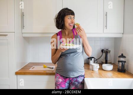 Buona donna incinta mangiare in cucina Foto Stock