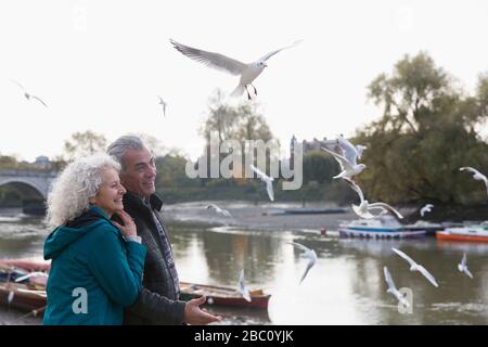 Affettuosa coppia senior guardando uccelli che volano al fiume Foto Stock