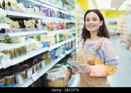 Ritratto sicuro, sorridente femmina drogheria con tablet digitale in supermercato Foto Stock