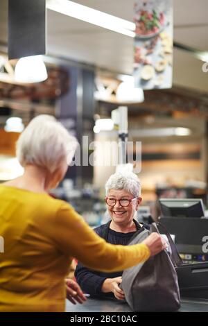 Cashier femminile gentile e senior che aiuta il cliente a effettuare il check-out al supermercato Foto Stock