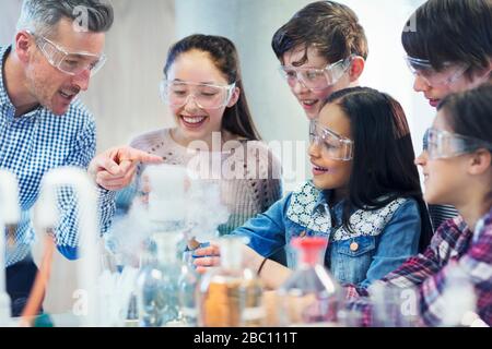 Insegnante di sesso maschile e studenti che osservano la reazione chimica, conducendo esperimenti scientifici in classe di laboratorio Foto Stock