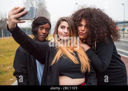 Tre giovani donne sportive che prendono selfie in città Foto Stock