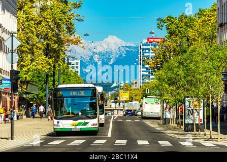 Lubiana - Settembre 2019, Slovenia: Vista di una strada con i mezzi pubblici, passeggiata a piedi, architettura moderna e le Alpi innevate sullo sfondo Foto Stock