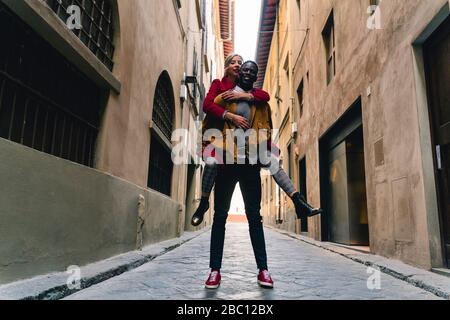 Felice giovane uomo che porta la ragazza piggyback in un vicolo nella città di Firenze, Italia Foto Stock