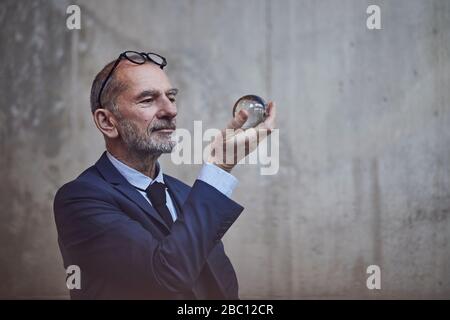 Uomo d'affari senior che guarda la palla di cristallo Foto Stock