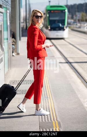 Donna d'affari bionda con abito rosso, in attesa del prossimo treno Foto Stock