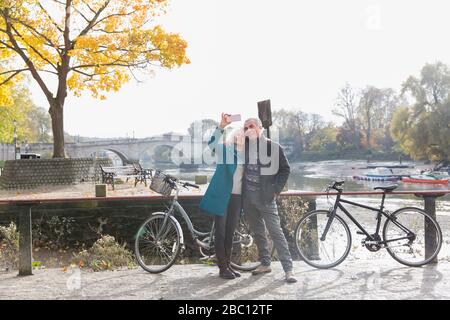 Coppia senior con biciclette che prendono selfie in autunno fiume Foto Stock