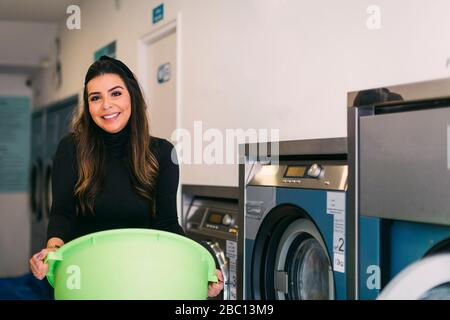 Ritratto di giovane donna sorridente che fa la lavanderia in un cestino di tenuta della lavanderia Foto Stock