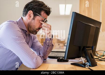 Stanco uomo d'affari alla scrivania in un ufficio open-space in legno Foto Stock