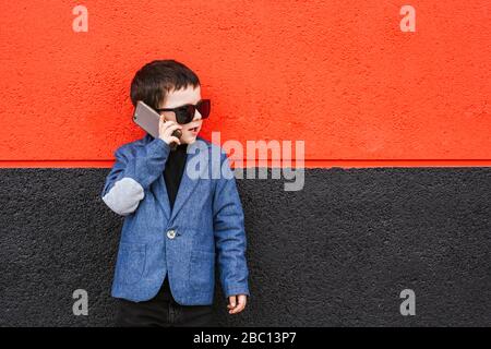 Ritratto di bambino sul telefono che indossa il cappotto e gli occhiali da sole oversize Foto Stock