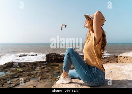 Giovane donna che gode di luce del sole vicino al mare, Essaouira, Marocco Foto Stock