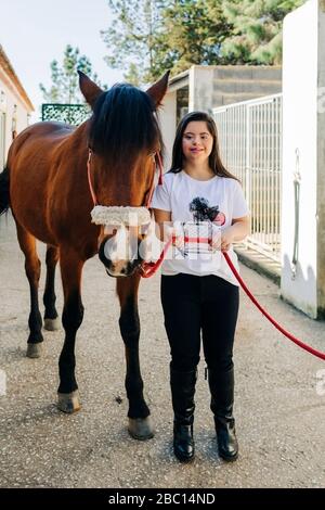 Adolescente con sindrome di Down prendersi cura del cavallo e preparare cavallo a cavalcare Foto Stock