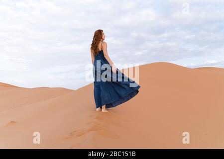 Giovane donna in piedi sulla duna di sabbia nel deserto del Sahara, Merzouga, Marocco Foto Stock