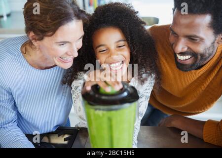 Famiglia multietnica ridente che fa i frullati verdi sani nel frullatore in cucina Foto Stock