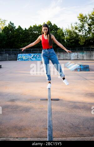 Giovane donna che si equilibrano su una rotaia allo skatepark Foto Stock