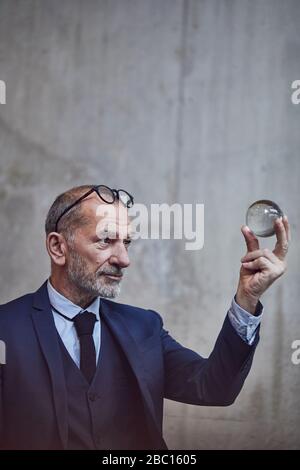 Uomo d'affari senior che guarda la palla di cristallo Foto Stock