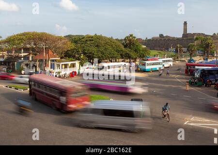 Traffico ad una rotonda vicino alla stazione centrale degli autobus Galle con la torre Galle Fort Clocktower visibile sullo sfondo, Galle, Sri Lanka Foto Stock