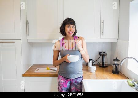 Ritratto donna incinta felice mangiare in cucina Foto Stock