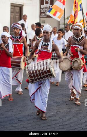 Uomini vestiti in stire tradizionale suonando tamburi durante un festival buddista a Galle, Sri Lanka Foto Stock