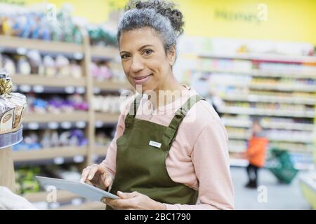 Ritratto sorridente, sicuro femmina drogheria con tablet digitale che lavora in supermercato Foto Stock