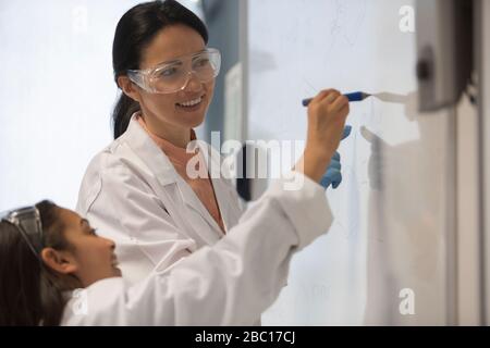 Insegnante di scienze femminili e studentessa studentesca che scrive alla lavagna in classe Foto Stock