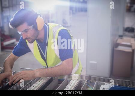 Tecnico specializzato che indossa cuffie protettive, assemblando le apparecchiature in fabbrica Foto Stock