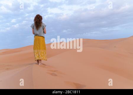 Giovane donna in piedi sulla duna di sabbia nel deserto del Sahara, Merzouga, Marocco Foto Stock