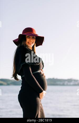 Ritratto di giovane donna incinta alla moda in piedi sul lungomare Foto Stock