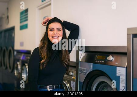 Ritratto di giovane donna sorridente che fa la lavanderia in una lavanderia Foto Stock