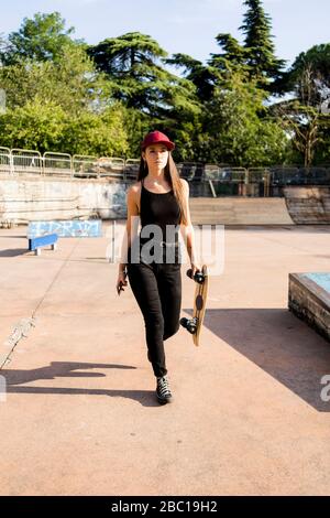 Giovane donna ha lo skateboard e smartphone in uno skatepark Foto Stock