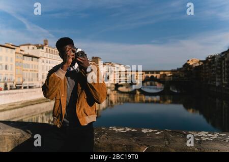 Giovane uomo che prende una foto su un ponte sopra il fiume Arno, Firenze, Italia Foto Stock