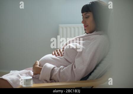 Serena donna incinta in accappatoio tenendo stomaco Foto Stock