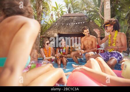Giovani amici che si aggrappano nella soleggiata piscina estiva Foto Stock