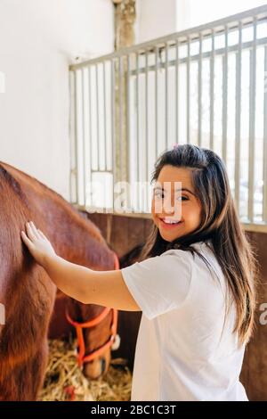 Adolescente con sindrome di Down prendersi cura del cavallo e preparare cavallo a cavalcare Foto Stock