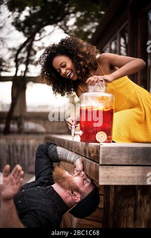 Donna felice che versa il tè di ghiaccio nella bocca del ragazzo Foto Stock