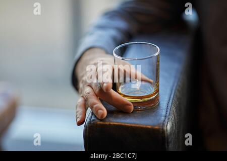 Primo piano di uomo con bicchiere di whiskey sul bracciolo di una sedia in pelle Foto Stock