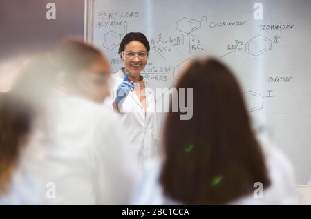 Sorridente insegnante di scienza femminile lezione di guida alla lavagna in classe Foto Stock