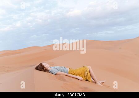 Giovane donna sdraiata in dune di sabbia nel deserto del Sahara, Merzouga, Marocco Foto Stock