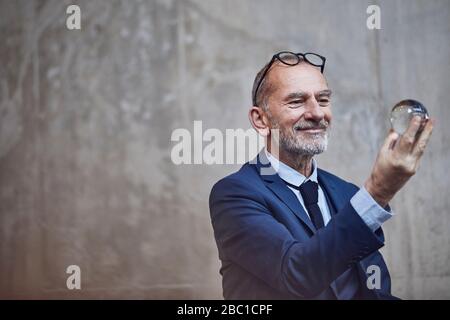 Uomo d'affari senior che guarda la palla di cristallo Foto Stock