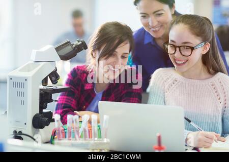 Insegnante e studentesse di sesso femminile con microscopio e laptop, conducendo esperimenti scientifici in classe di laboratorio Foto Stock