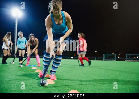 Determinato giovane giocatore di hockey da campo femminile praticando sport trivella sul campo di notte Foto Stock