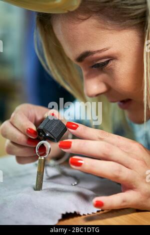 Donna che controlla un anello di diamante attraverso una lente di ingrandimento Foto Stock