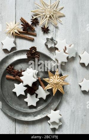 Biscotti a forma di stella, bastoncini di cannella, coni di pino, tagliatubi, piatto di peltro, anice stellato e decorazioni natalizie in paglia Foto Stock